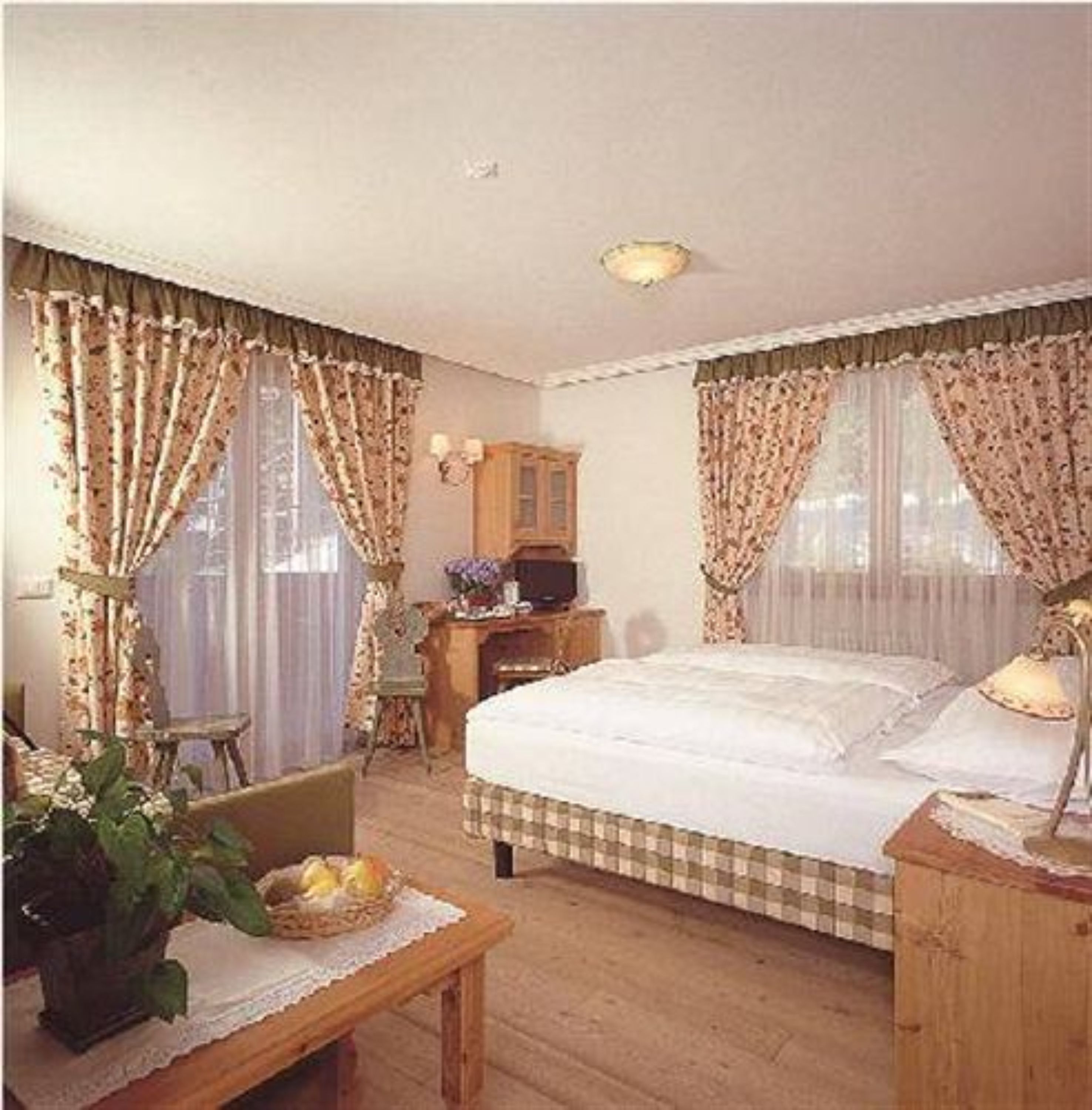 A bedroom with a large bed, a wooden dresser, a desk, and a chair.