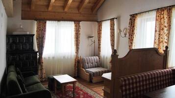 Een gezellige kamer met een houten plafond, een groene bank, een gestreepte fauteuil, een bankje en een kleine tafel.