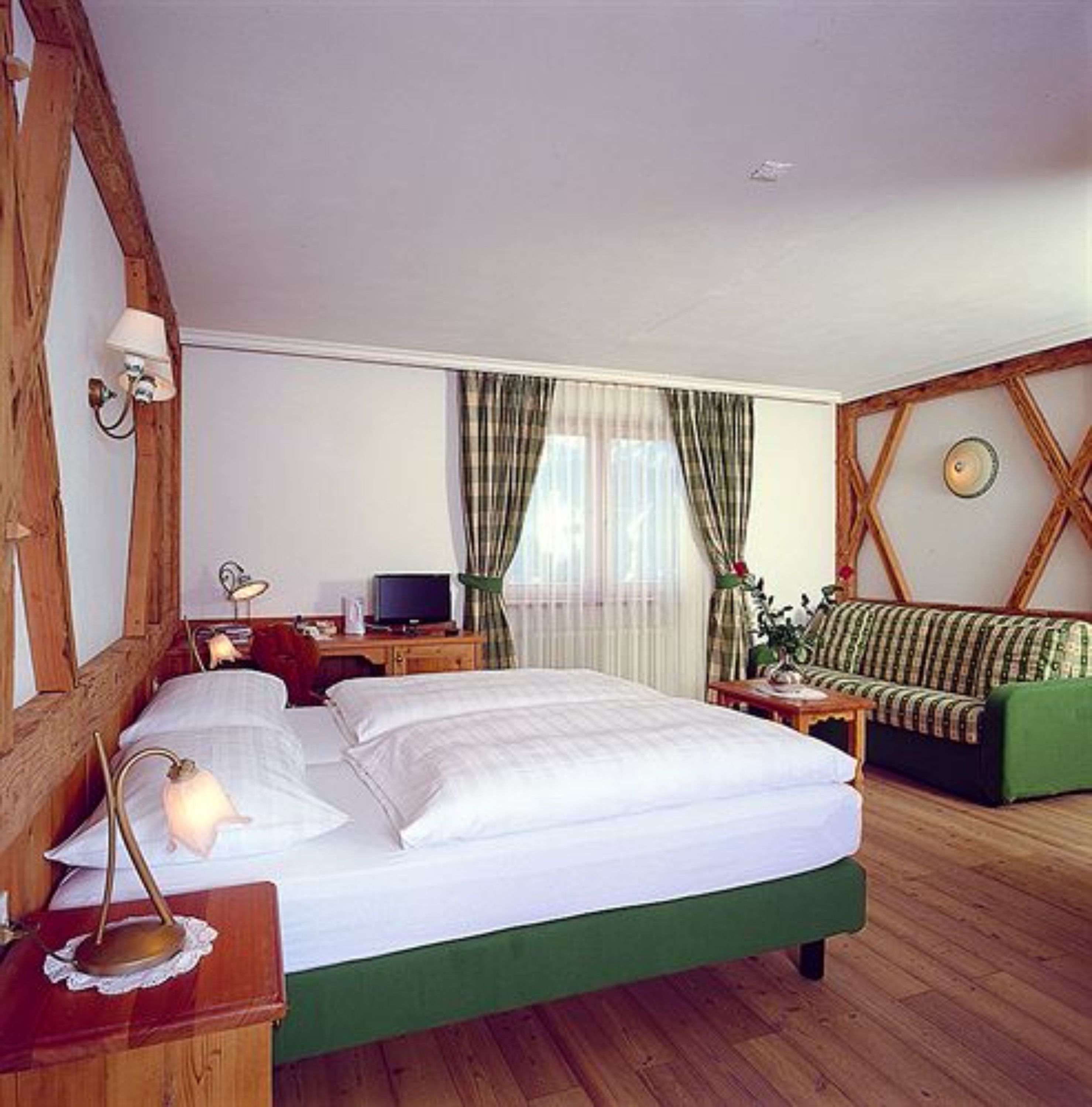 A room with a bed, a desk with a computer, a green sofa, and a window with curtains.