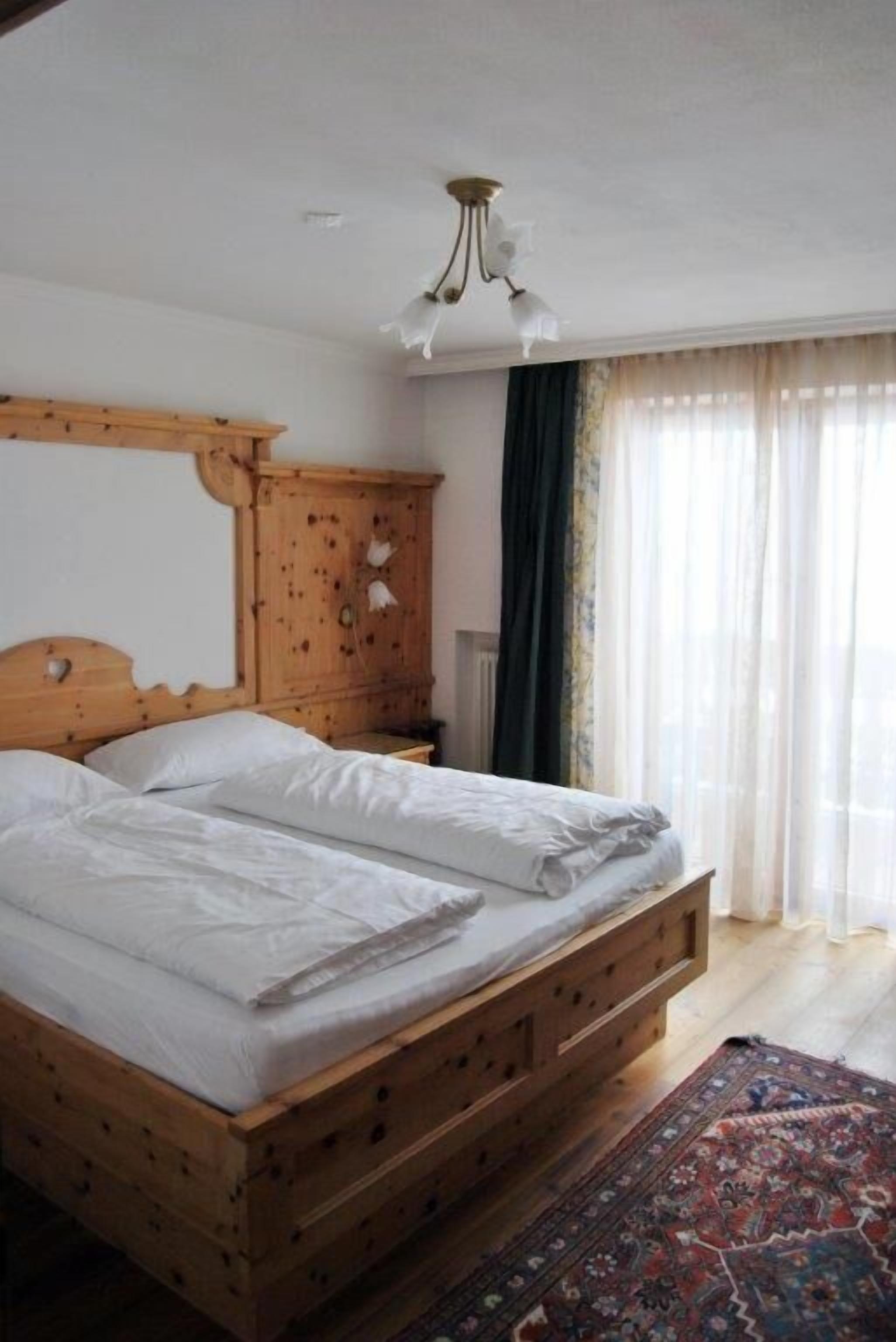 A bedroom with a wooden bed, a nightstand, a wardrobe, and a large window with curtains.