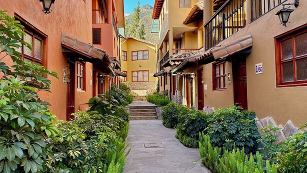 A narrow alleyway flanked by buildings with balconies, stone steps leading to a door, and lush greenery. - Hotel Mabey Urubamba (Urubamba)