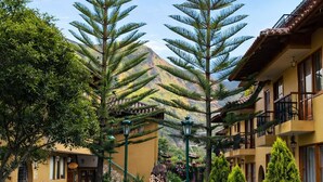 A pathway lined with tall trees and a building with balconies and outdoor seating. - Hotel Mabey Urubamba (Urubamba)