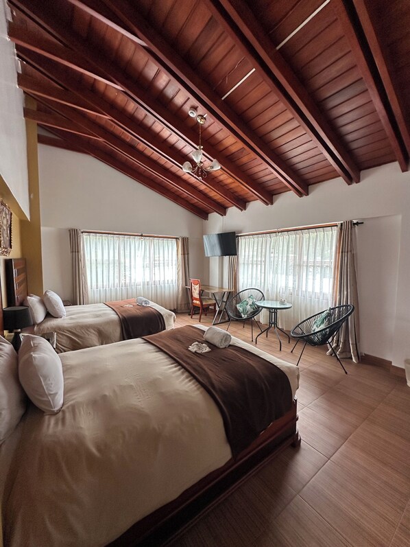 Habitación de hotel con dos camas, una mesa de comedor, televisión y ventilador de techo.