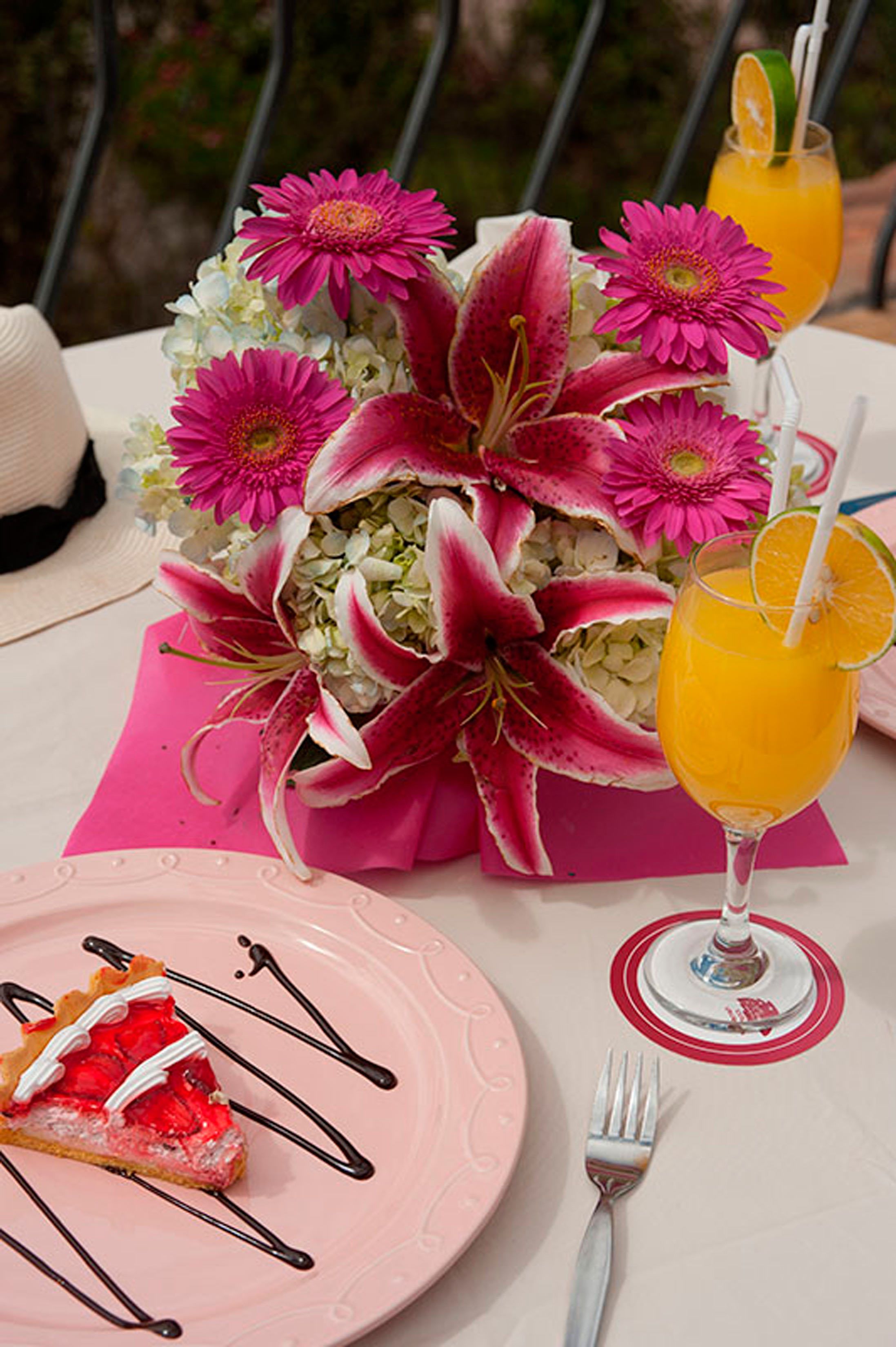A table with a pink plate of pie, a glass of orange juice, and a bouquet of flowers.
