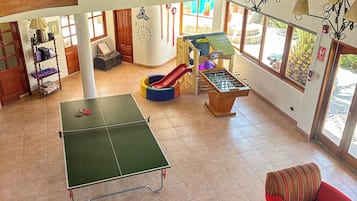 Un espacio interior amplio con mesa de ping pong, mesa de fútbol de mesa, tobogán y un sofá rojo.