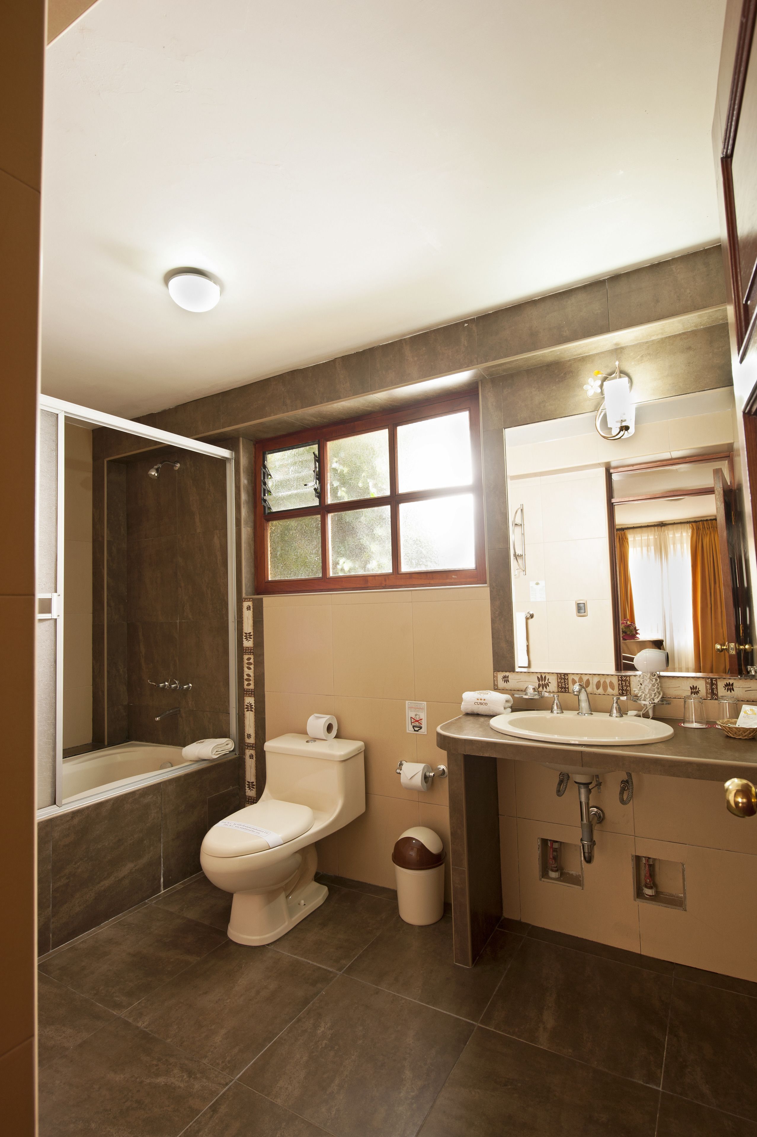 Un baño con bañera, inodoro, lavamanos y una ventana con cortinas.