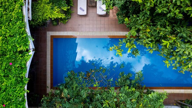 An aerial view of a swimming pool surrounded by lush greenery, with two sun loungers and a tiled deck area. - Skyline Boutique Hotel (Phnom Penh)