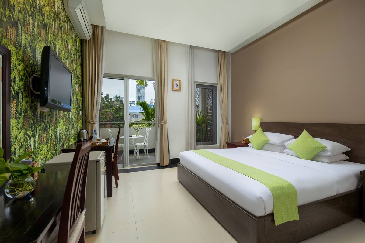 Una camera d'albergo con un letto, una scrivania, una sedia, una televisione e un balcone con vista sulla città.