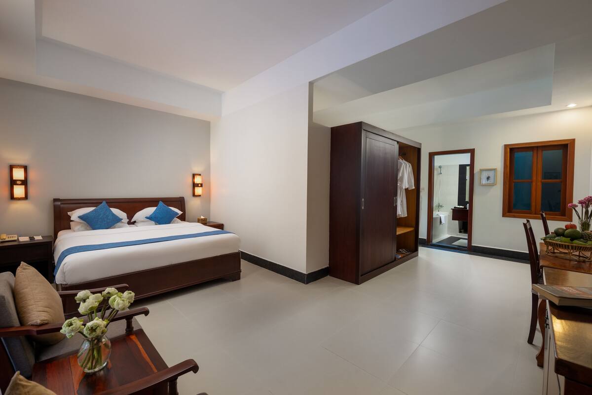 Camera d'albergo con un letto, un comodino e una scrivania con una sedia. Si nota un armadio e un bagno attraverso una porta aperta.