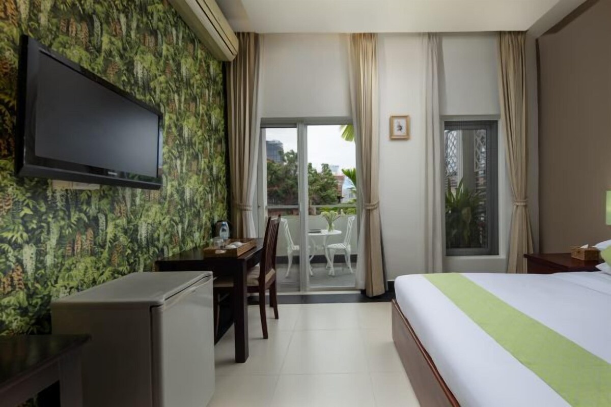 A hotel room with a bed, a desk, a television, and a balcony with a view of the city.
