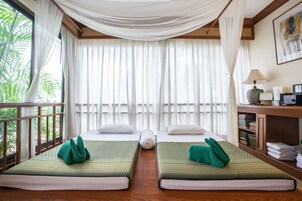 Habitación con dos camas, un escritorio con lámpara y vistas a la vegetación a través de amplias ventanas.