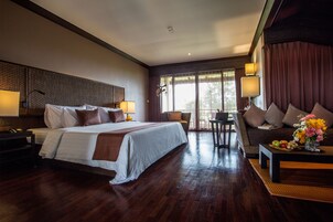 Habitación de hotel con una cama grande, un sofá, una mesa de comedor con fruta y vistas al exterior.