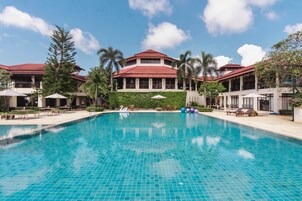 Una piscina con borde de baldosas, rodeada de zonas de descanso y palmeras.