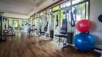 A gym with various exercise machines, large windows, and wooden flooring.
