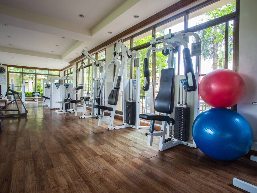 A gym with various exercise machines, large windows, and wooden flooring.