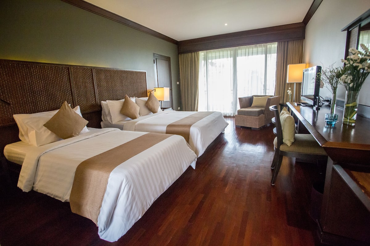 A hotel room with two beds, a desk, a chair, a TV, and a window with curtains.