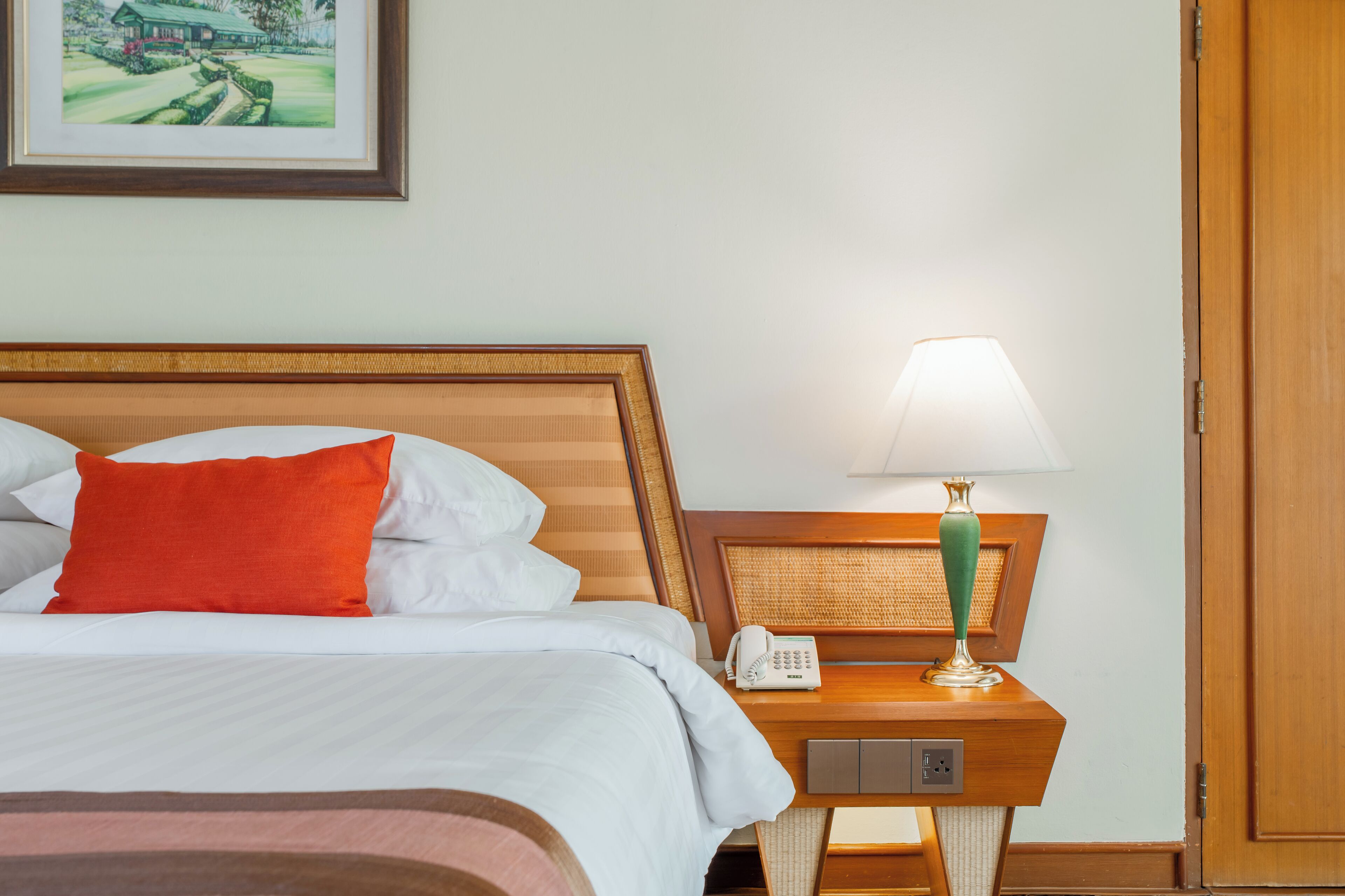 A hotel room with a bed, a nightstand with a lamp, a phone, and a framed picture on the wall.