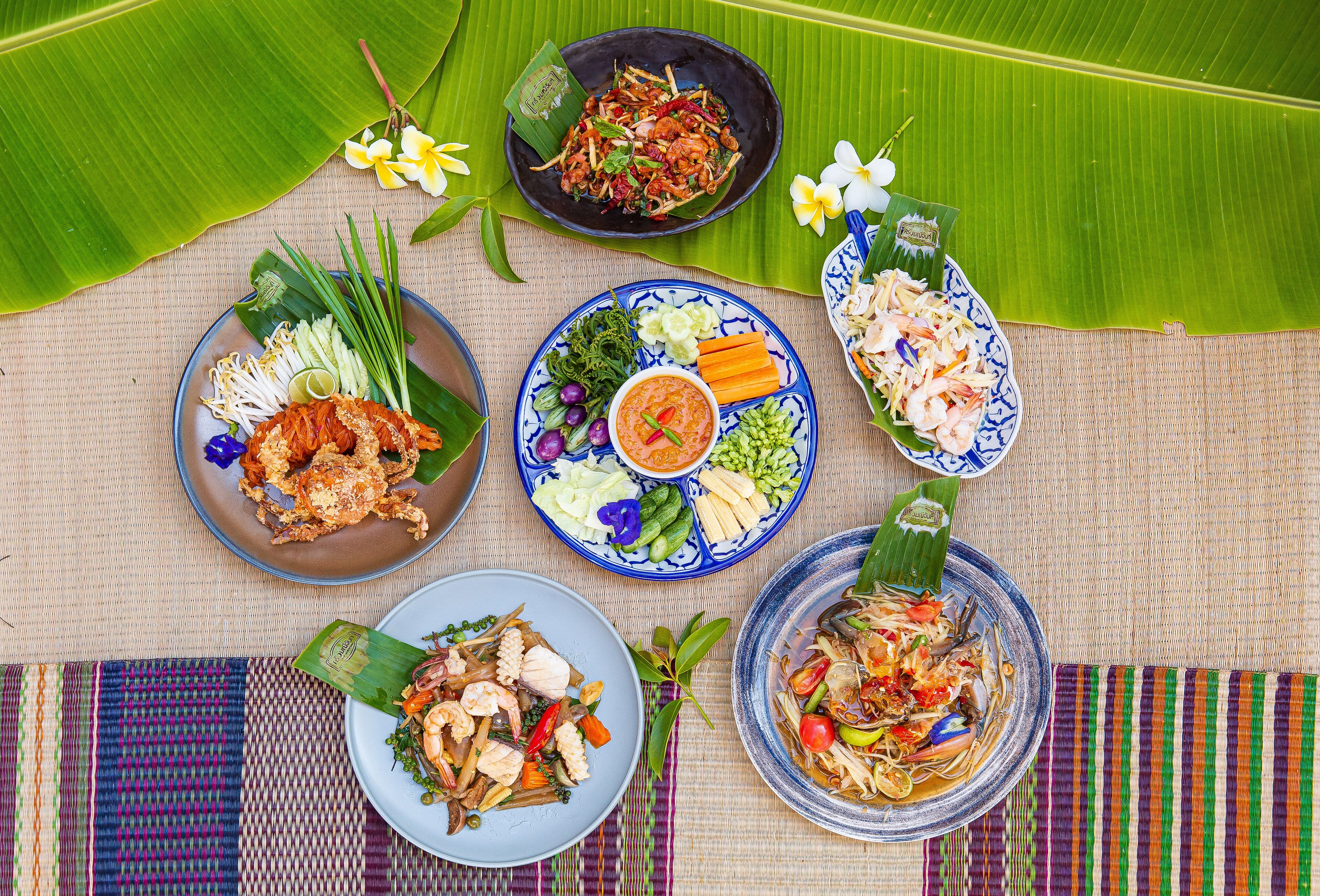 A table with various dishes, including seafood and vegetables, arranged on a woven mat with a banana leaf.