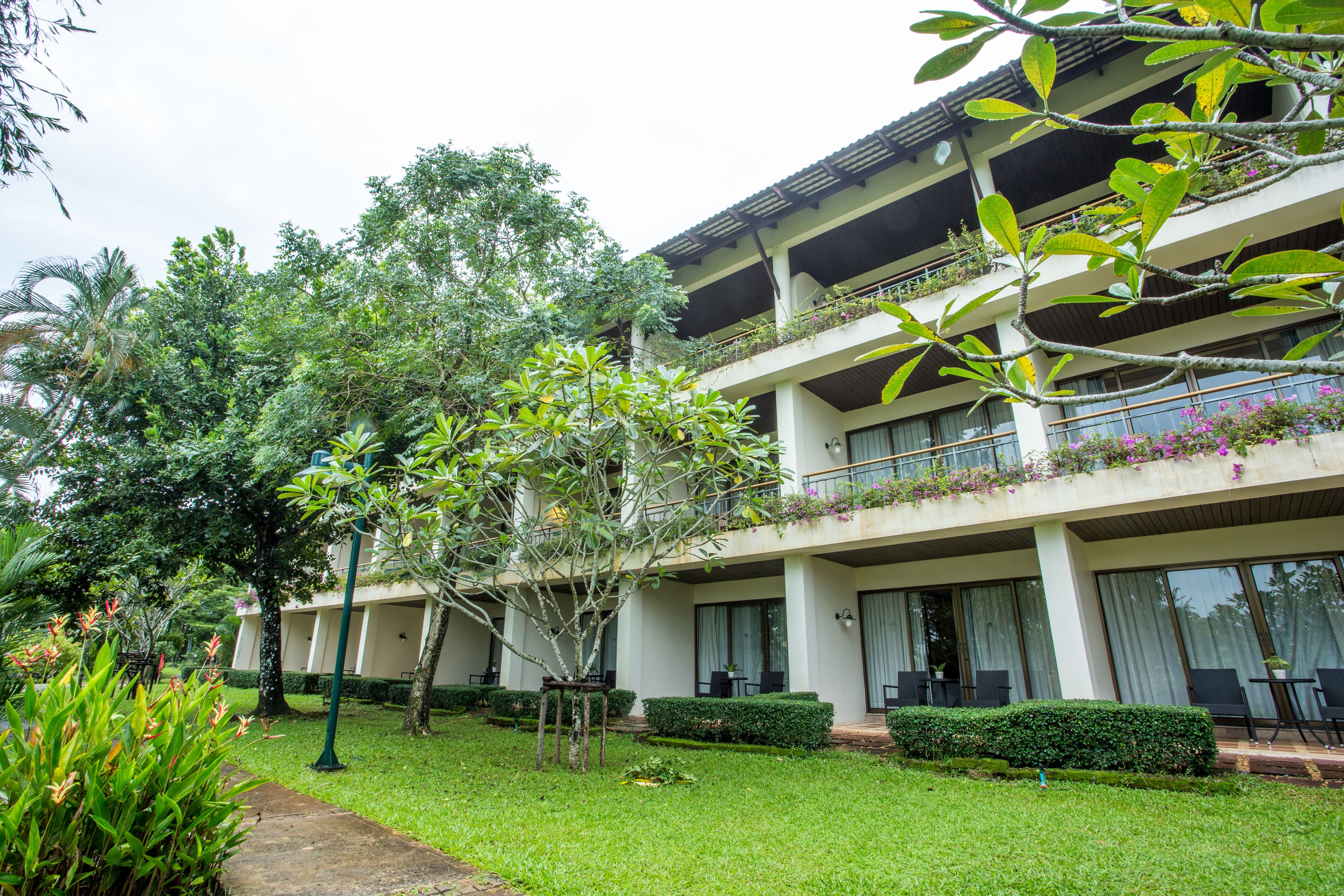 A hotel with a two-story structure, balconies with plants, and a well-maintained garden.