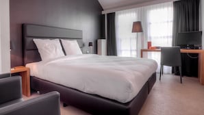 A modern hotel room with a large bed, a desk with a computer, and a chair. - Saint James (Mons)