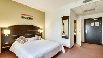 Een hotelkamer met een groot bed, bedlampen, een wandspiegel en een deur met slot.
