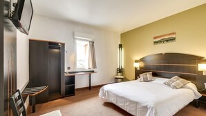 Une chambre d’hôtel comprenant un lit, un bureau, une chaise, une armoire et un téléviseur.