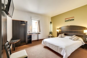 Habitación de hotel con cama, escritorio, silla, armario y televisor.