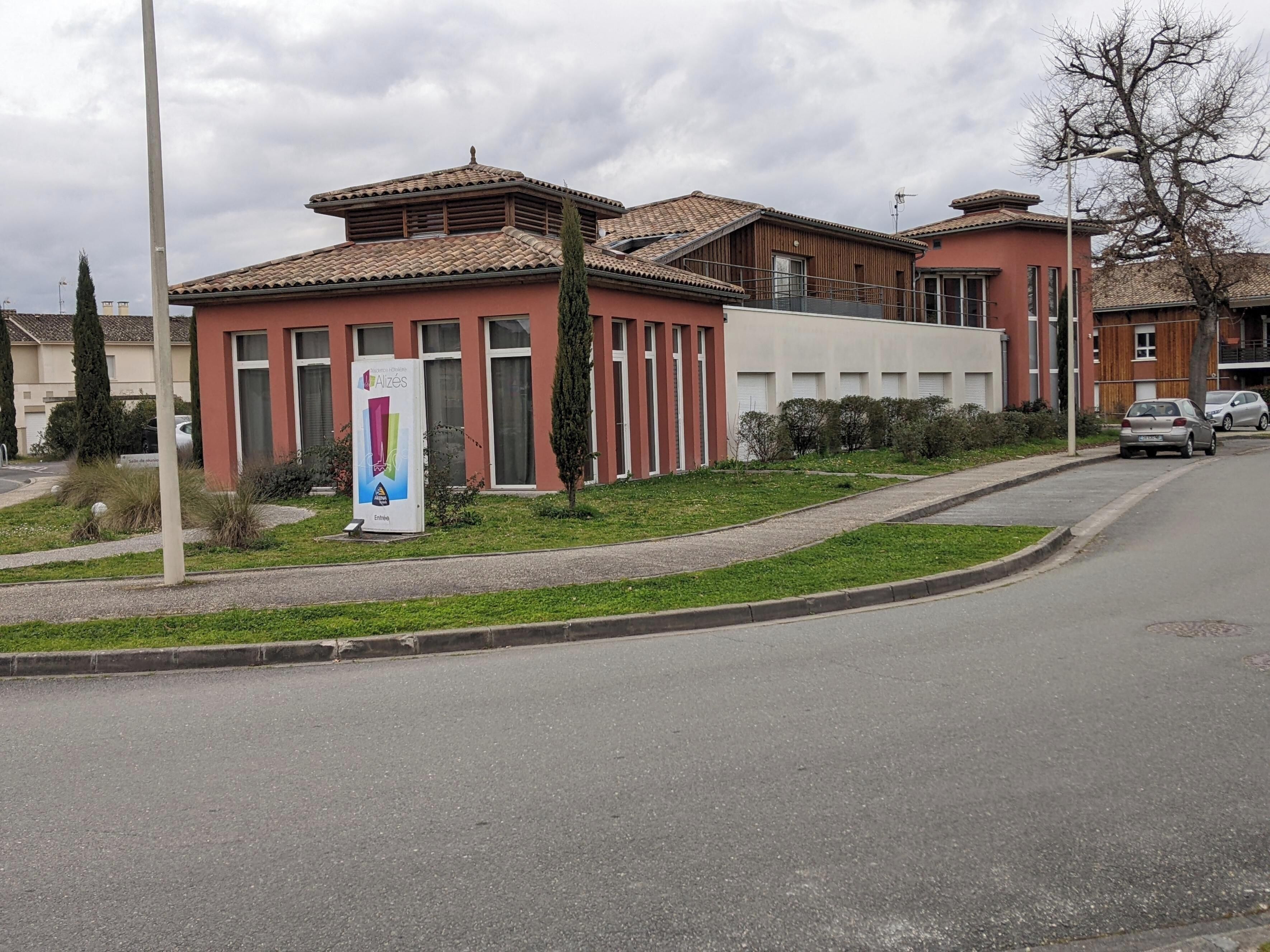 A building with a tiled roof, a signboard, and a road with parked cars.