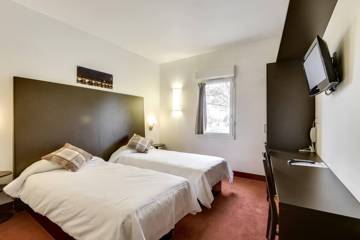 A hotel room with two beds, a desk, a television, and a window with curtains.