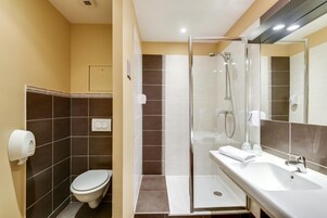 Un baño con inodoro, ducha con puerta de vidrio y lavabo con espejo.