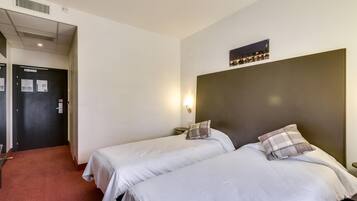 Habitación de hotel con dos camas, un cabecero oscuro, una lámpara de pared y un cuadro enmarcado sobre las camas.