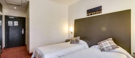 Habitación de hotel con dos camas, un cabecero oscuro, una lámpara de pared y un cuadro enmarcado sobre las camas.