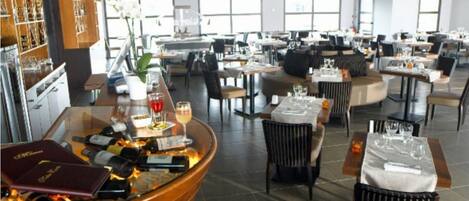A spacious restaurant with high ceilings, large windows, and a variety of seating arrangements including tables and chairs.