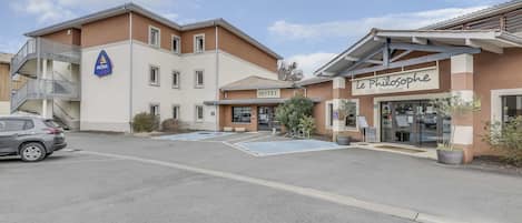 A hotel with a sign for 'Le Philosophe' cafe and restaurant, a staircase, and a parking area.
