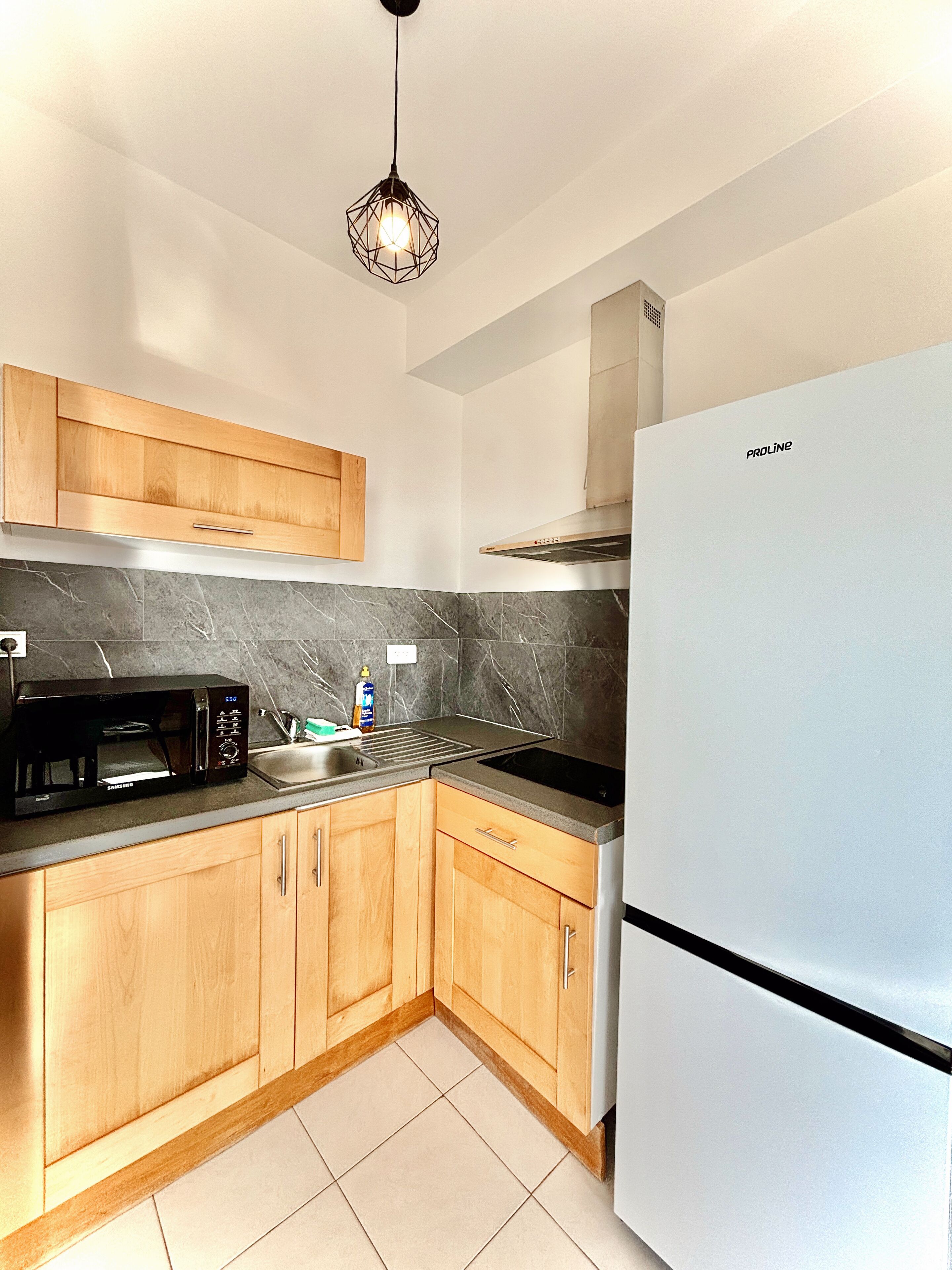 A modern kitchen with wooden cabinets, a black microwave, a stainless steel sink, and a white refrigerator.
