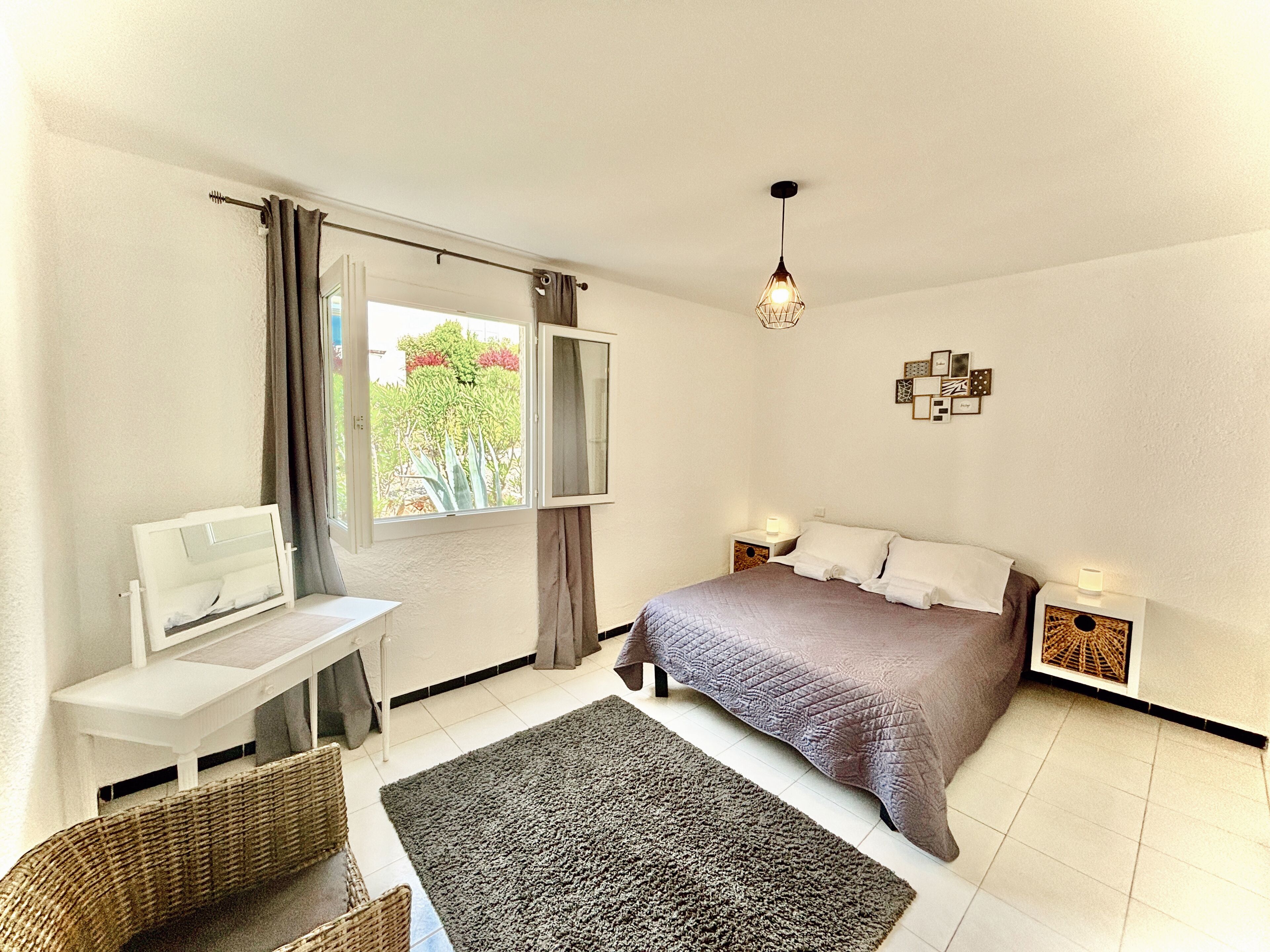 A bedroom with a bed, a desk, a chair, a window with curtains, and a bedside table with a lamp.