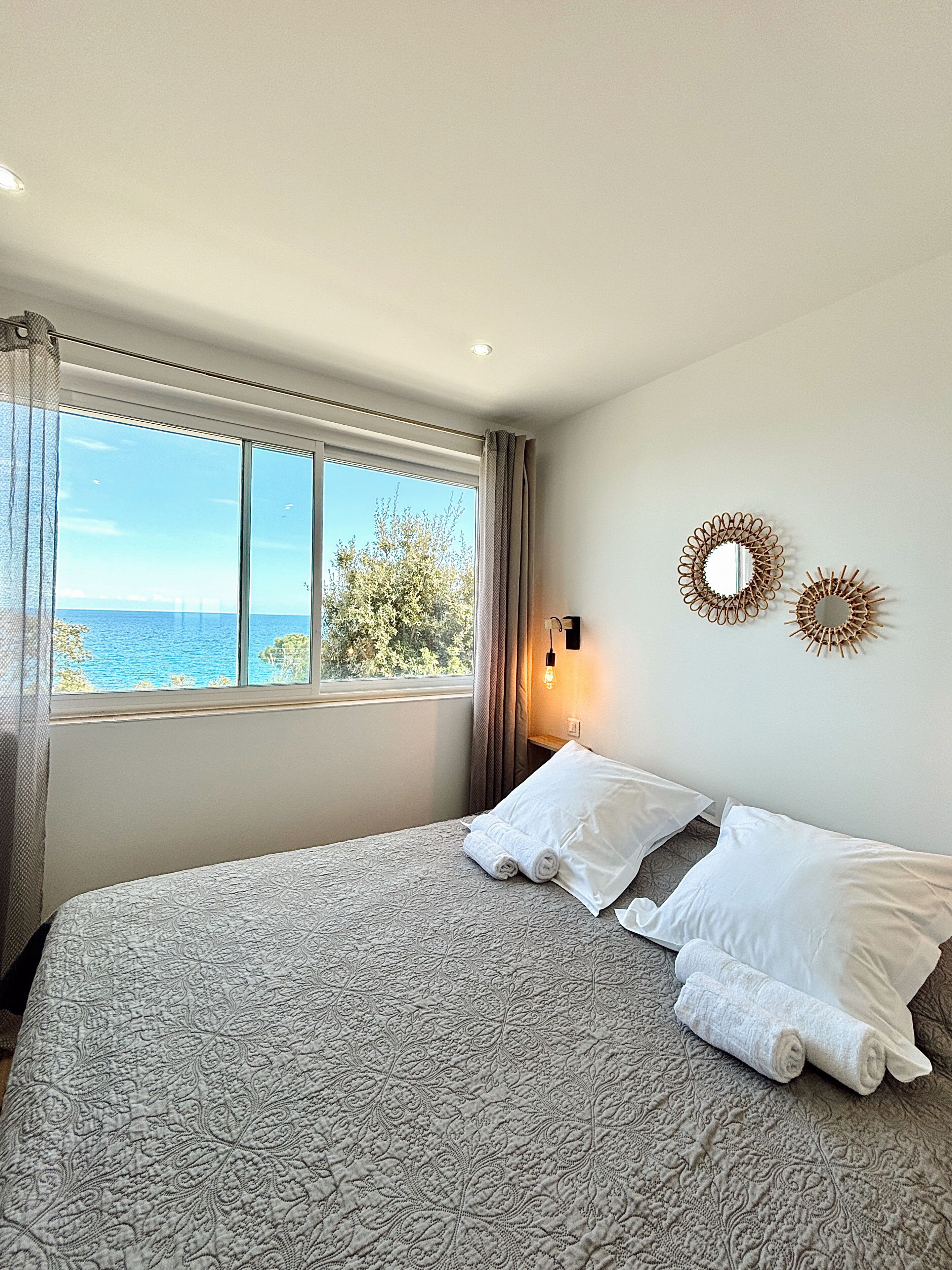 Un dormitorio con una cama grande, vista al mar y dos espejos colgados en la pared.