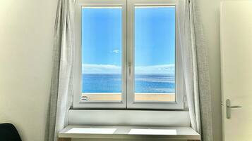 A room with a window overlooking a beach, a white door, and a black chair.