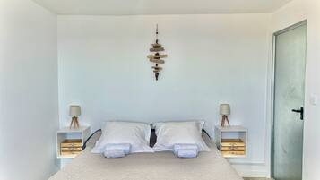 Une chambre à coucher bien rangée, avec un lit placé au centre, entre deux tables de chevet, chacune ornée d’une lampe et d’une boîte en bois.
