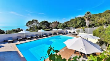 Una piscina al aire libre, sombrillas, sillones reclinables de piscina