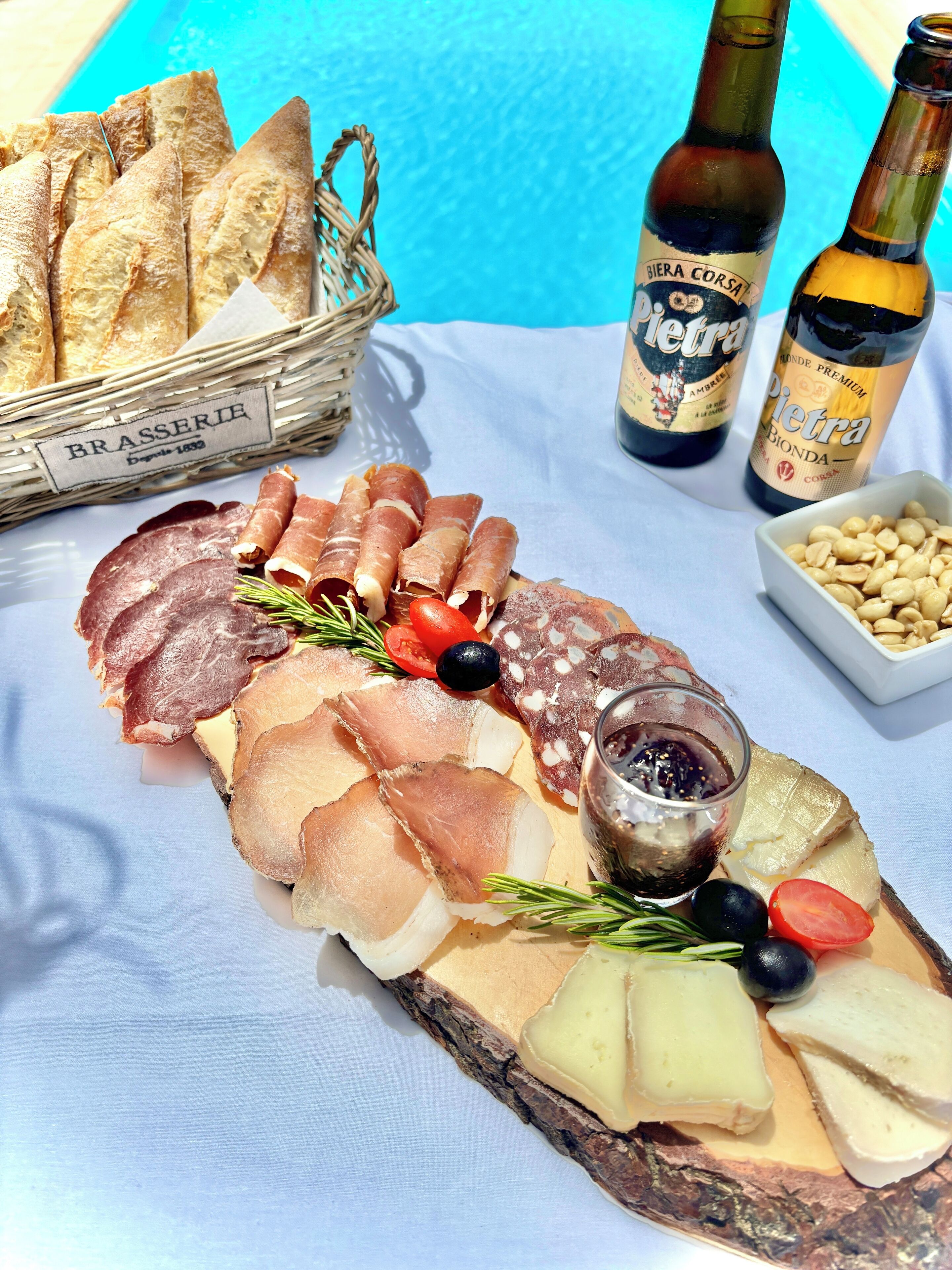 A charcuterie board with various meats, cheeses, olives, and bread, accompanied by bottles of beer.
