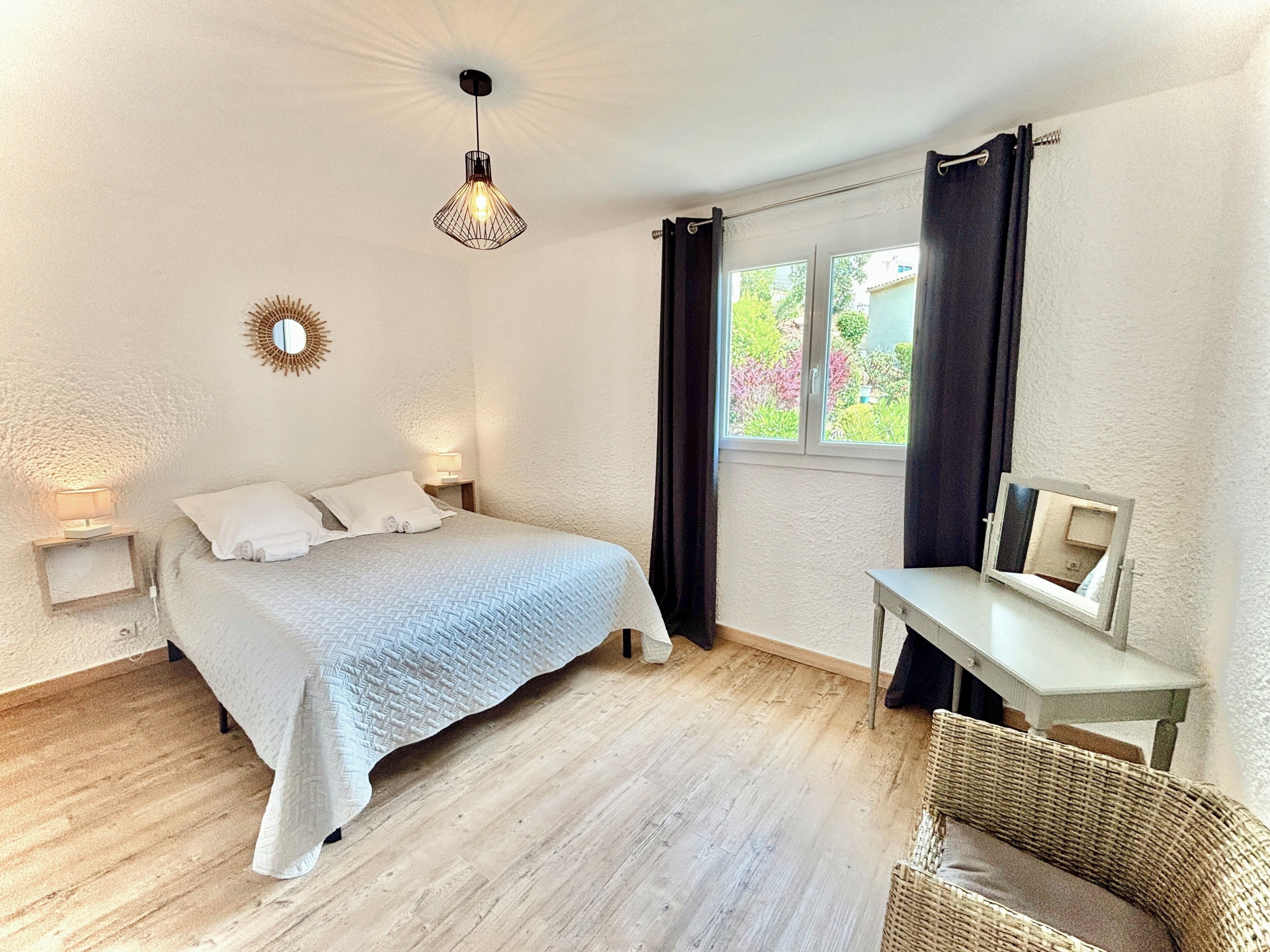 A bedroom with a bed, bedside lamps, a small table with a mirror, and a wicker chair.