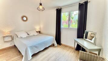 Un dormitorio con cama, lámparas de noche, una mesita con espejo y una silla de mimbre.