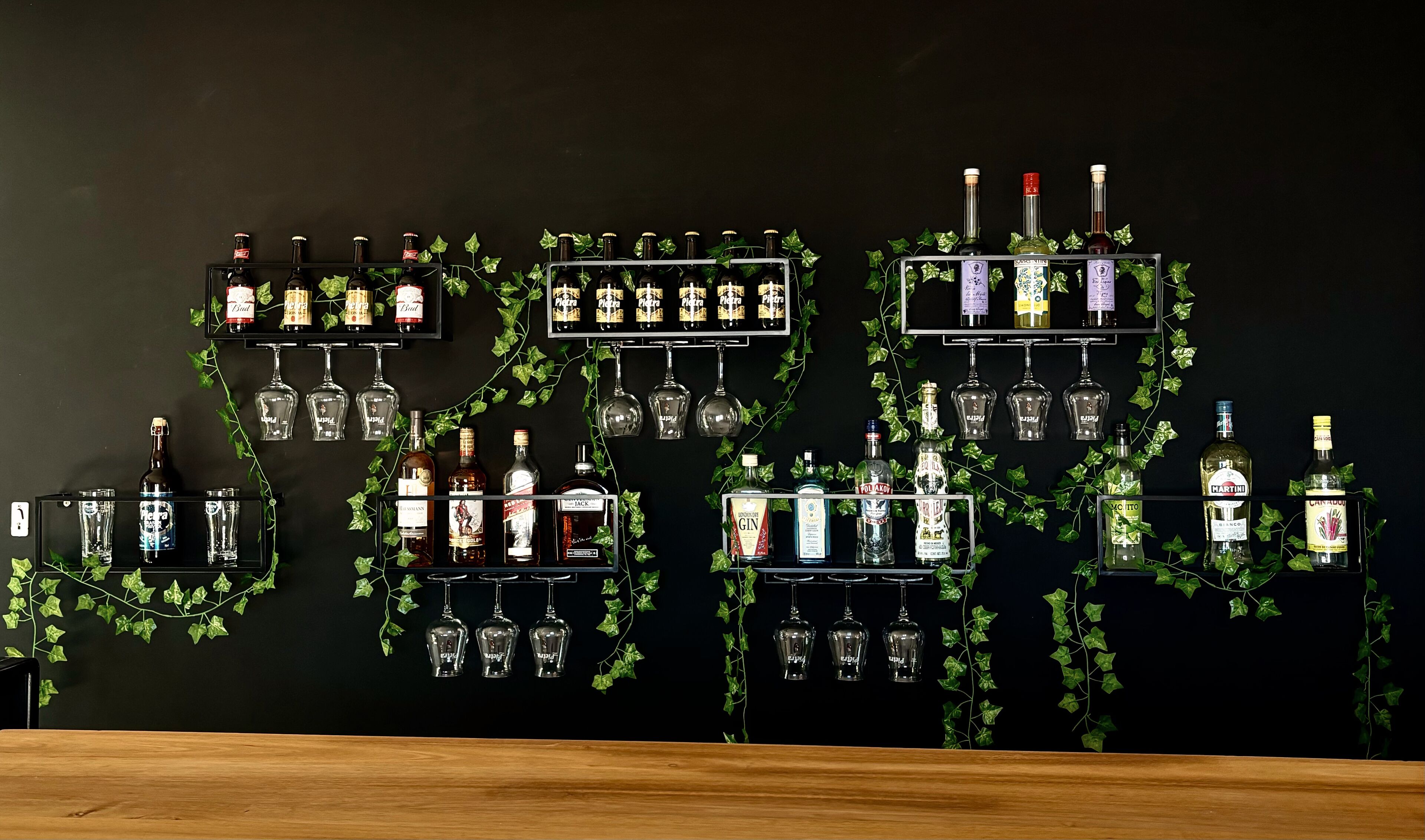 A wall with multiple shelves displaying various bottles and glasses, some with labels and some without.
