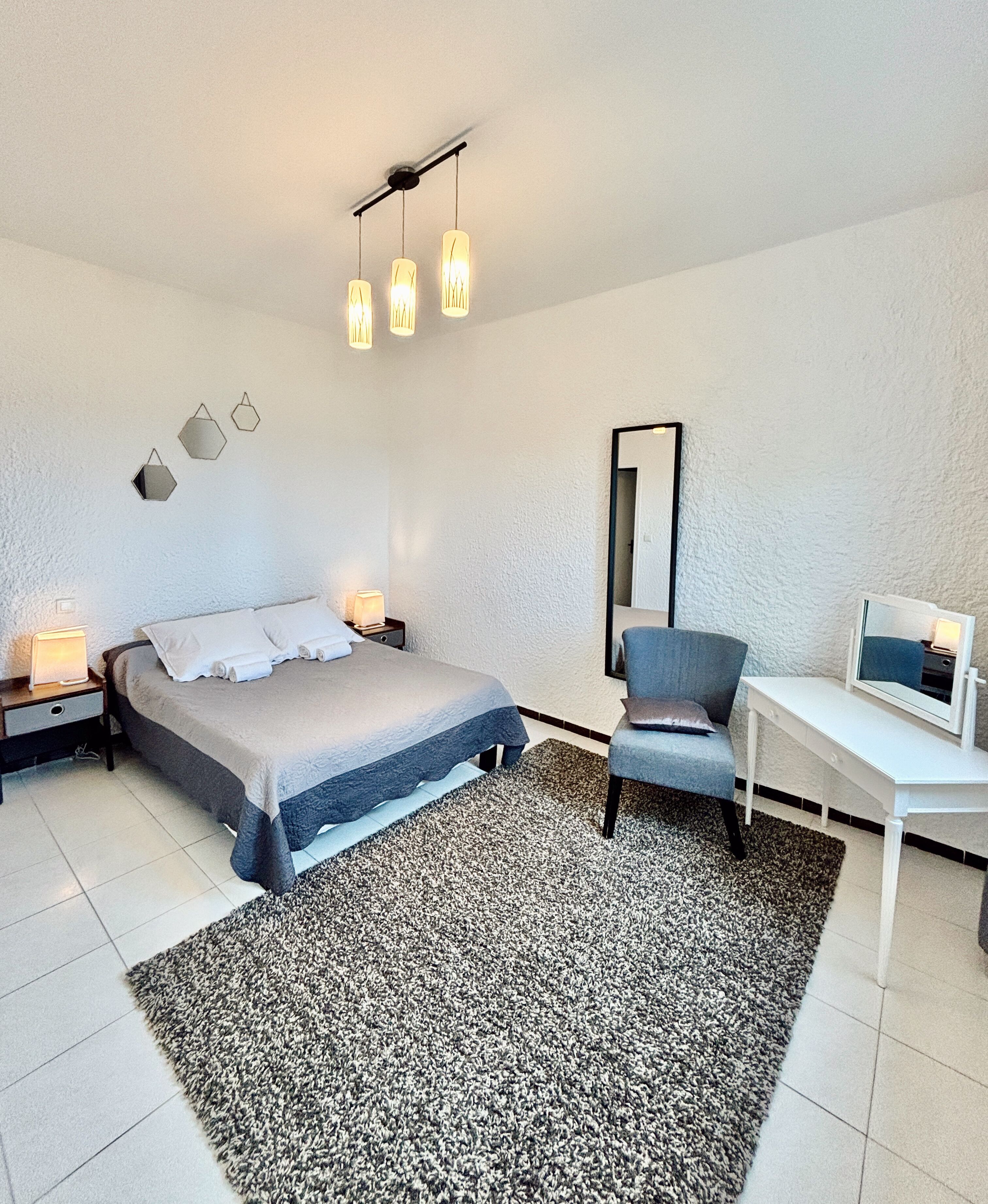 A modern bedroom with a bed, bedside tables, a desk, a chair, a rug, and a mirror.