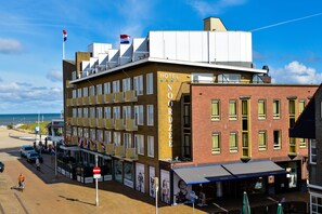 A hotel with a prominent 'HOTEL NOORDZEE' sign, a balcony with yellow railings, and a view of the beach. - Hotel Noordzee (Katwijk Aan Zee)