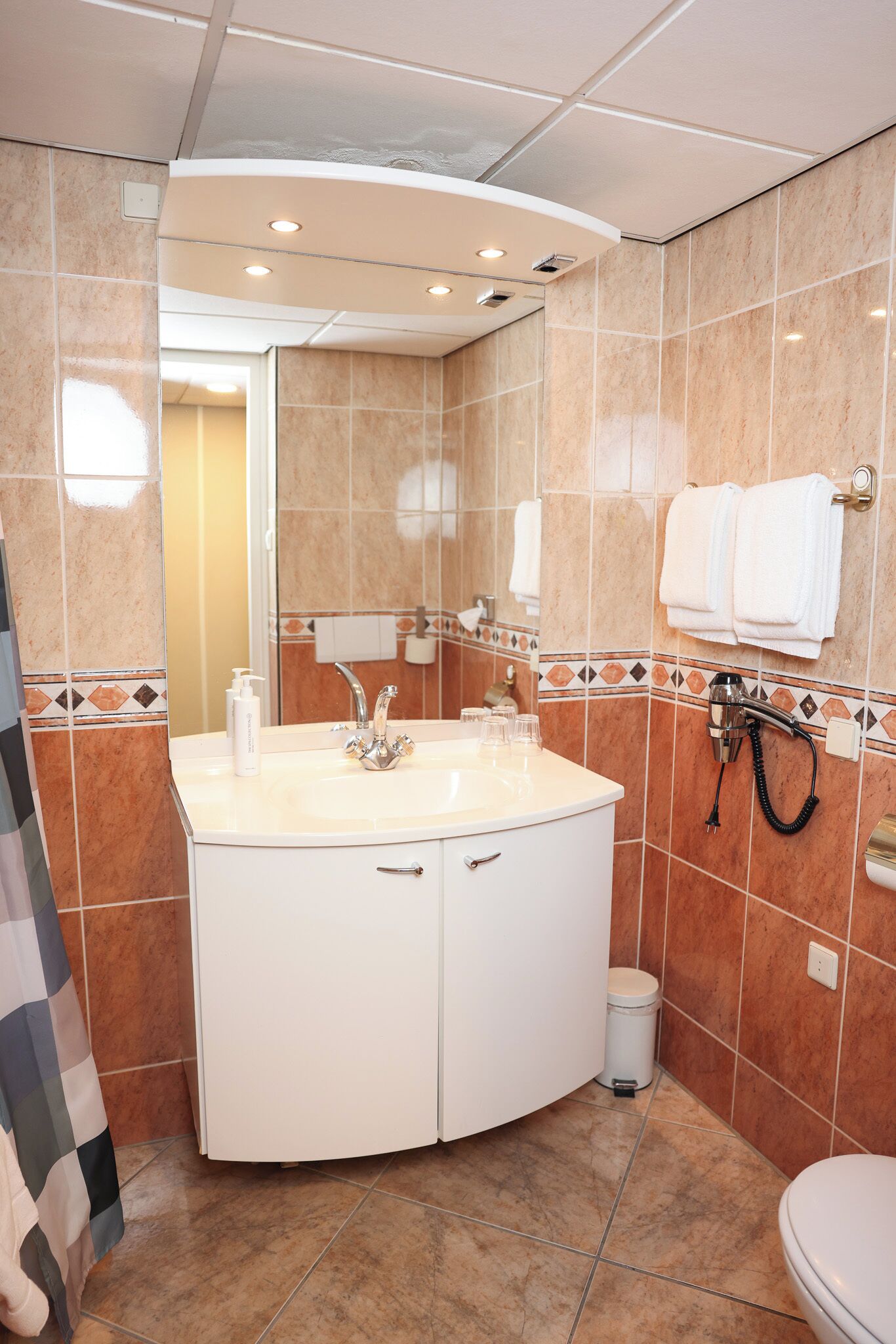 Een badkamer met een gebogen wit wastafelmeubel, een spiegel, een handdoekrek en een douchehoek.