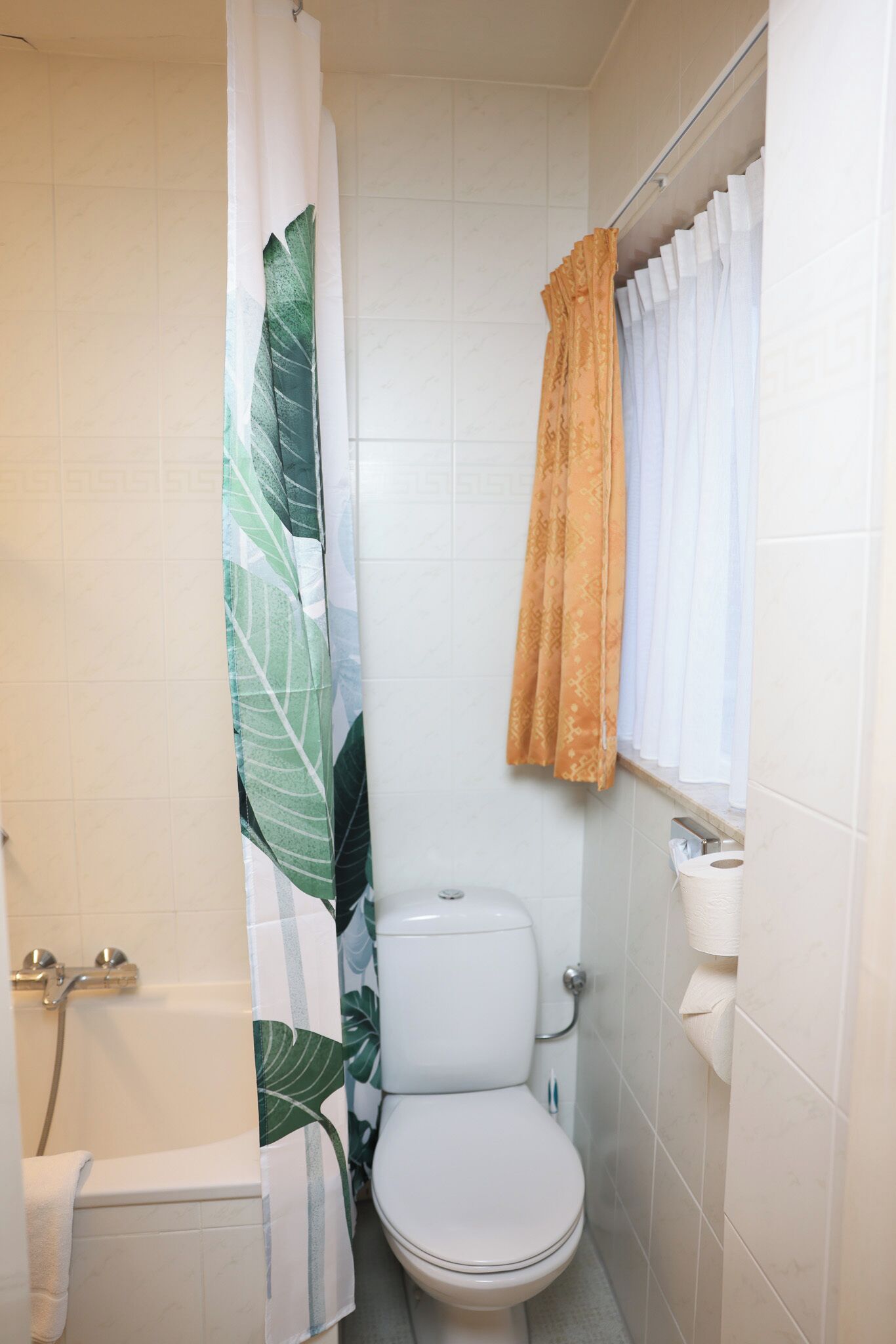 Un baño pequeño con inodoro, cortina de ducha y ventana con cortina.