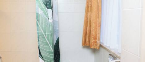 Un baño pequeño con inodoro, cortina de ducha y ventana con cortina.