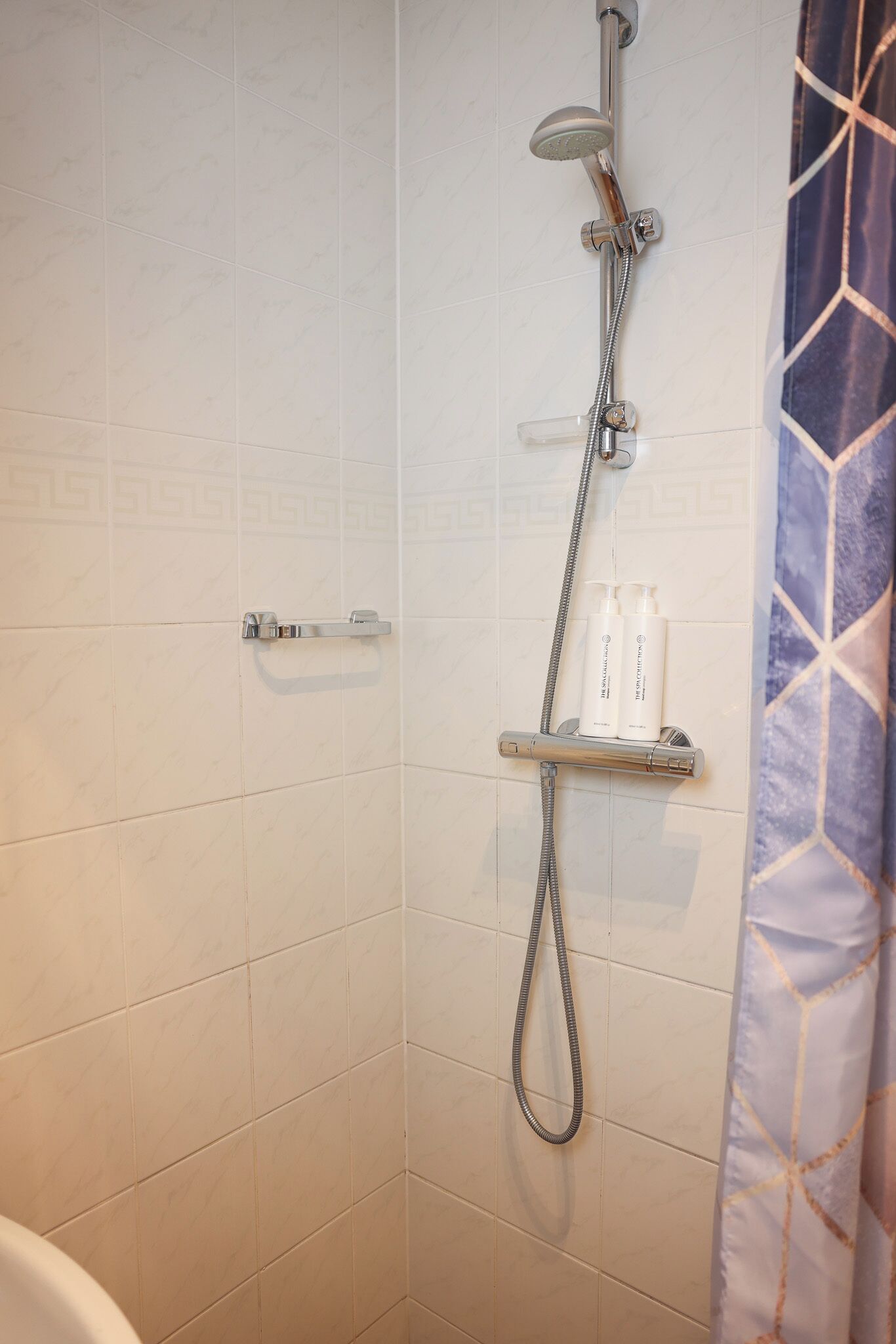 A shower area with a handheld showerhead, a wall-mounted faucet, and a shelf holding two bottles.